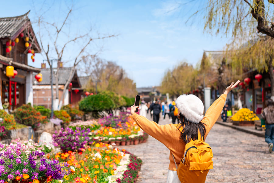 Una turista con mochila disfrutando de las calles empedradas y decoradas con flores de un pueblo antiguo en Yunnan; una muestra de las experiencias auténticas de nuestros viajes personalizados a China.